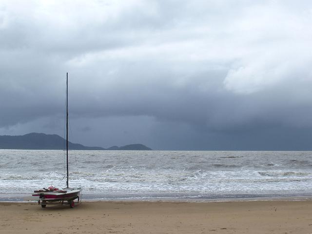 a sailing dinghy sat by a stormy sea scape, dunk island