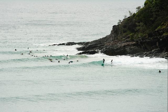 Surfers in the sea at Noosa beach, Australia riding the waves at the bottom of a rocky headland as they wait for a roller to catch a ride