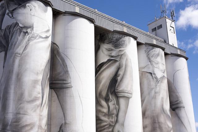 Closeup of large decorated grain silos in Coonalpyn, South Australia with murals of men drawn on the facades against a blue sky