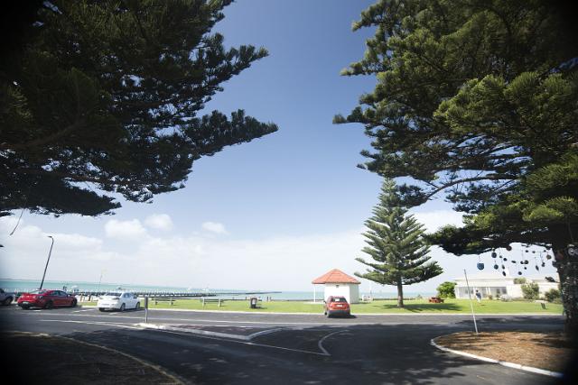 The beachfront at Beachpoint, Rivoli Bay, Australia with a view between coniferous trees of a large parking lot and distant ocean