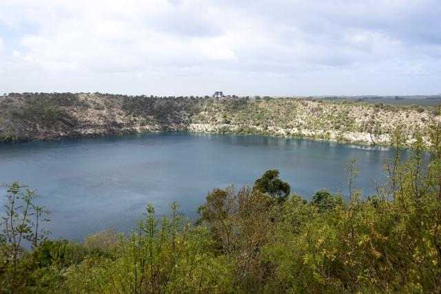 Blue Lagoon, or Blue Lake, in a volcanic crater at Mt Gambier, South Australia viewed over greenery and trees in a scenic landscape with cloudy sky