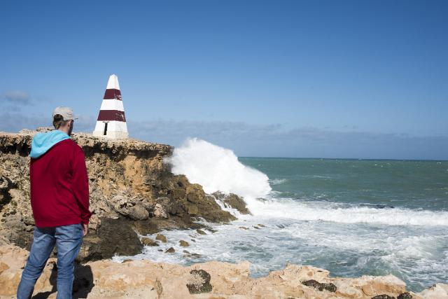 Obelisk at Cape Dombey, Rode, Australia with breaking waves over the cliff and a man standing on the rocks in the foreground viewing it