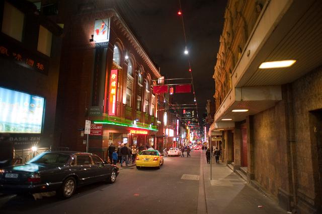 Street scene in China Town in Melbourne at night with bright colourful neon signs, cars and pedestrians