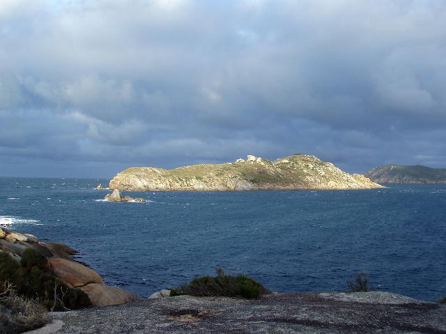 wattle island bathed in sun against a dark stormy background, south point, wilsons promontory