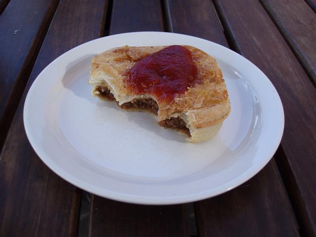 the australian national dish, a half eaten meat pie with tomato sauce