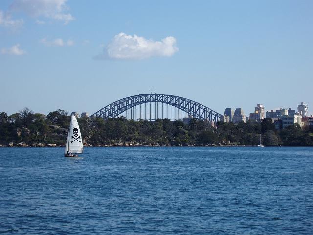 a boat sailing on sydney harbour with the top of the harbour bridge in the distance