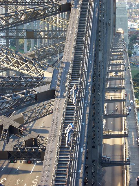 pedestrians and traffic crossing sydney harbour bridge as people climbing the bridge look down from above