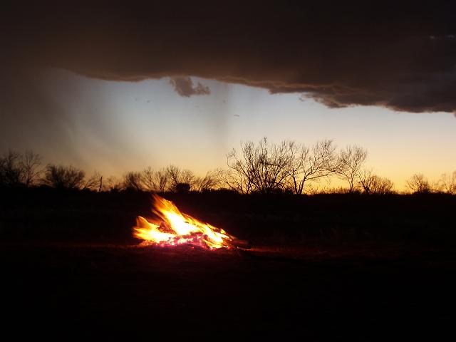 a camp fire at sunset with passing cloud and rain shower