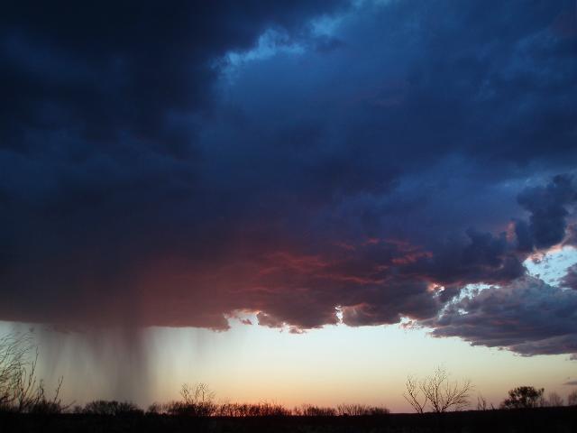 a heavy dark storm cloud dropping rain onto the desert floor at sunset
