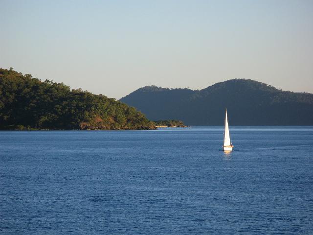 a boat sailing through the whitsunday islands, late in the day on a sunny evening