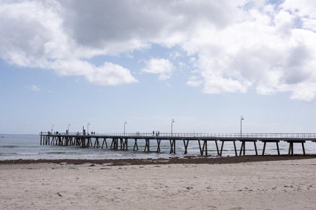 The beachfront pier in Glenelg, Adelaide, Australia with a deserted sandy beach in the foreground on a cloudy blue sky day
