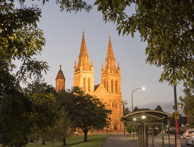 Street view of St Peters Cathedral, Adelaide, Australia at dusk illuminated from the front with a bus stop and street lights in the foreground