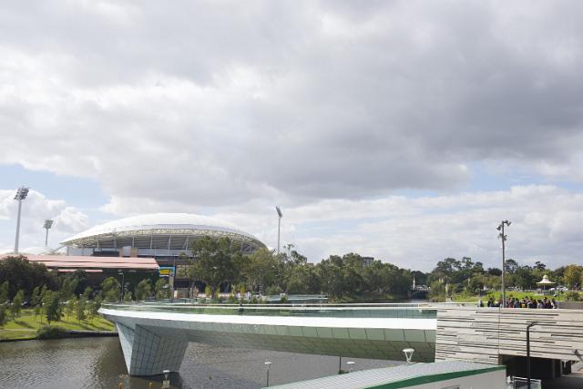 Bridge over water at the Stella Brown Park, Adelaide, Australia with the Adelaide Cricket Oval visible over green shrubs behind