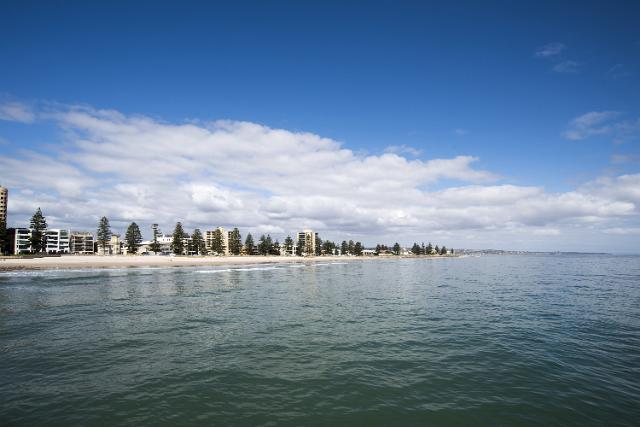 Waterfront coastline with a long sandy beach lined with trees and apartment buildings, Glenelg, Adelaide, Australia, viewed across the water of the bay