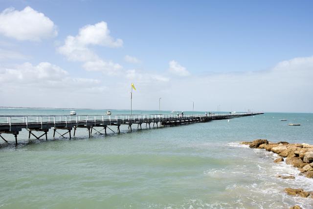The boardwalk pier at Beachport, South Australia extending far out into the ocean with distant people enjoying a stroll and boats out to see